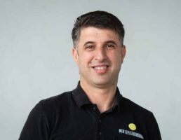 _DSC5539 Lächelnder Mann mit dunklem Haar trägt ein schwarzes Polo mit der Aufschrift Der Elektroman.